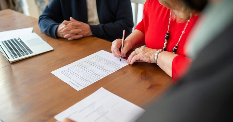 A woman signs a contract in an office with lawyers present, symbolizing intellectual property agreements.