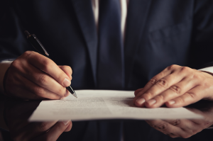 A man signs paperwork at a table.